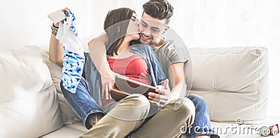 Happy couple having fun buying clothes online their baby - Husband and wife laughing and having tender moments - Main focus on man Stock Photo