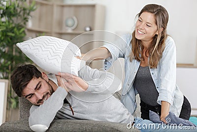 Happy couple jokingly holds pillow fight on sofa Stock Photo