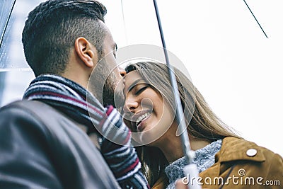 Happy couple kissing under an umbrella in a rainy day - Handsome man kiss his forehead girlfriend under the rain Stock Photo