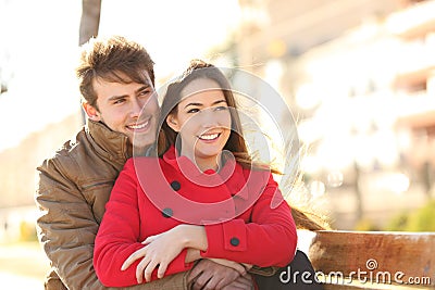 Happy couple looking away in winter on a bench Stock Photo