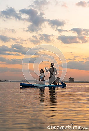 Happy couple paddle boarding at lake during sunset together with pug dog. active family tourism Stock Photo