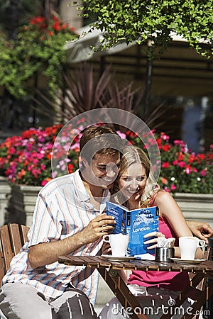 Happy Couple Reading Guidebook At Outdoor Cafe Stock Photo