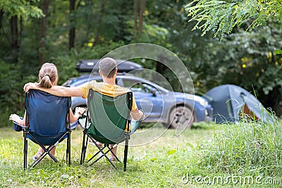 Happy couple sitting on chairs at campsite hugging together. Travel, camping and vacations concept Stock Photo