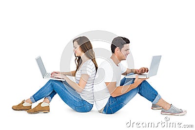 Happy couple sitting on the floor back to back using laptop Stock Photo