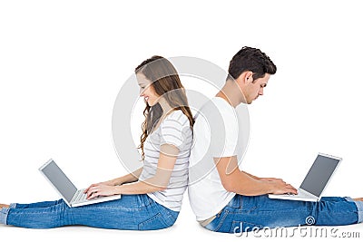 Happy couple sitting on the floor back to back using laptop Stock Photo