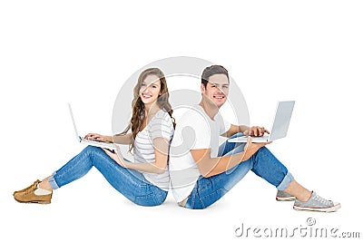 Happy couple sitting on the floor back to back using laptop Stock Photo