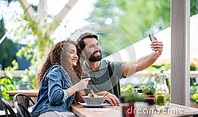 Happy couple sitting outdoors on terrace restaurant, taking selfie. Stock Photo