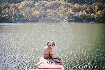 Happy couple sitting on a wooden bridge near lake Stock Photo