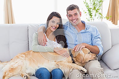 Happy couple stroking dog while sitting on sofa Stock Photo