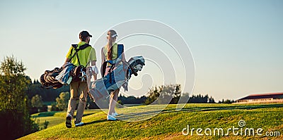 Happy couple wearing golf outfits while carrying stand bags Stock Photo