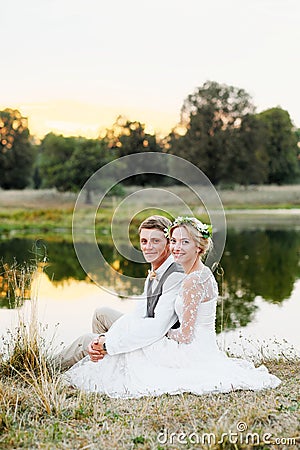 Happy couple in wedding attire on lake background at sunset, the bride and groom in a white dress. Stock Photo