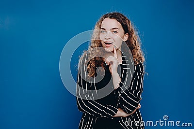 happy curly girl who came up with a good idea on a blue background in a striped jacket Stock Photo