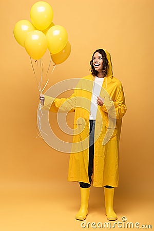 Happy curly woman in yellow raincoat and wellies holding balloons Stock Photo