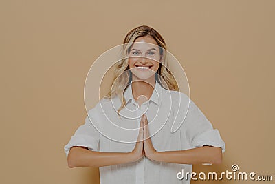 Happy cute blond girl in white shirt pressing palms together in pray or please gesture Stock Photo