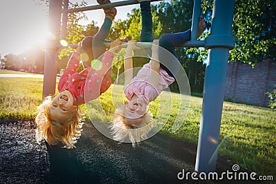 Happy cute little girls upside down on monkey bars at sunset Stock Photo