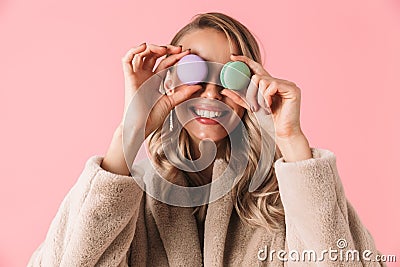 Happy cute young pretty woman posing over pink wall background holding cake macaroons sweeties Stock Photo