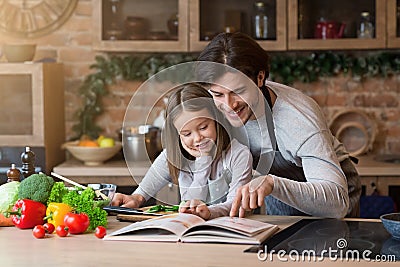 Happy dad and little daughter checking recipe in cookbook together Stock Photo