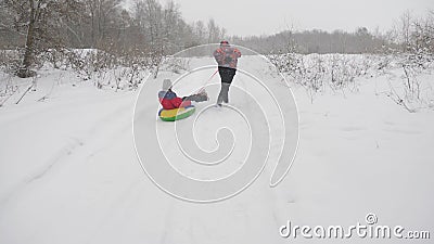 Happy dad sledges a child on a snowy road. Christmas Holidays. father plays with his daughter in a winter park. The Stock Photo