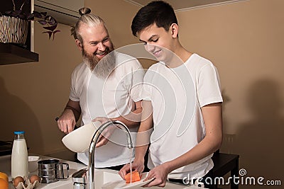 Happy dad and son on kitchen. Smiling father cooking, son washing the dishes. Friendly relationship of parents and teens Stock Photo