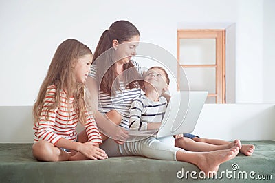 Happy delightful family consisting of mother and kids with laptop on knees Stock Photo