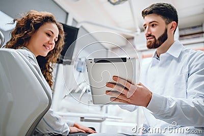 Happy dentist and patient commenting treatments in a tablet application in a consultation with medical equipment in the background Stock Photo