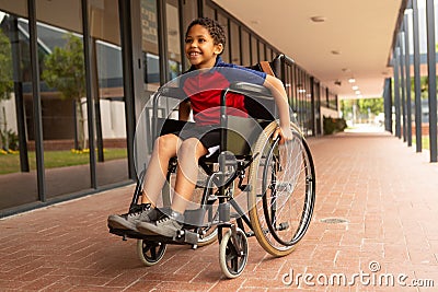 Happy disabled schoolboy sitting on wheelchair in corridor Stock Photo