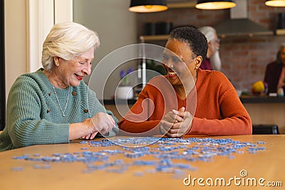 Happy diverse senior female friends playing with jigsaw puzzles in sunny dining room at home Stock Photo