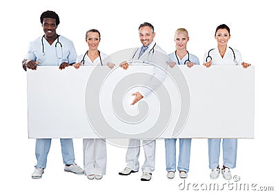 Happy Doctor Presenting Blank Billboard While Standing With Team Stock Photo