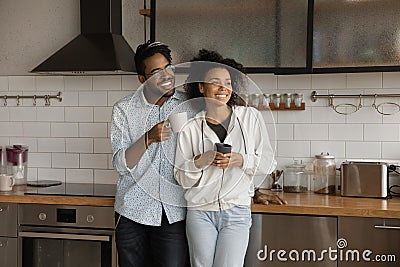 Happy dreamy African American couple drinking hot beverages in kitchen Stock Photo