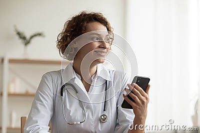 Happy dreamy young doctor looking in distance, holding mobile phone. Stock Photo