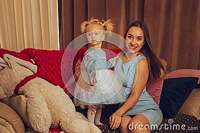 Happy dressy mom with her little baby girl sits on the couch Stock Photo