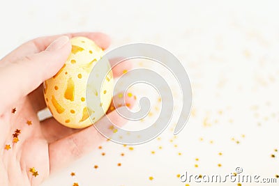 Happy Easter background. Closeup handpainted white egg with gold design in female hand with gold stars on white Stock Photo