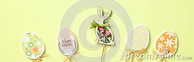 Happy Easter banner. Modern Easter eggs and rabbit decorations on wooden sticks on pastel green background Stock Photo