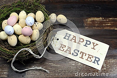 Happy Easter candy easter eggs in birds nest on dark vintage recycled wood with tag Stock Photo