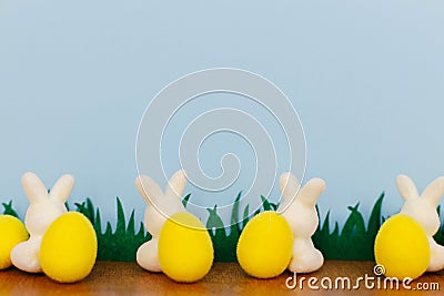 Happy Easter! Colorful Easter bunnies and eggs in grass on blue background with space for text. White and yellow artificial decor Stock Photo
