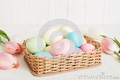 Happy Easter composition. Easter eggs in basket on colored table with yellow Tulips. Natural dyed colorful eggs Stock Photo