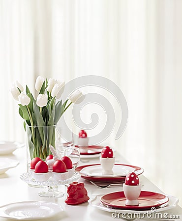 Happy easter. Decor and table setting of the Easter table is a vase with white tulips and dishes of red and white color. Easter Stock Photo