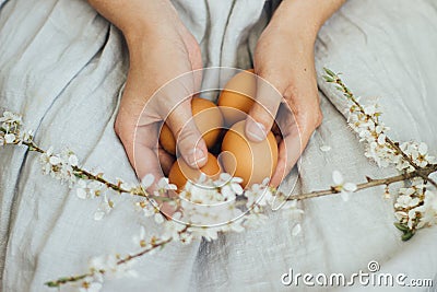 Happy Easter! Easter eggs and spring flowers in hands of woman in rustic linen dress. Aesthetic Stock Photo