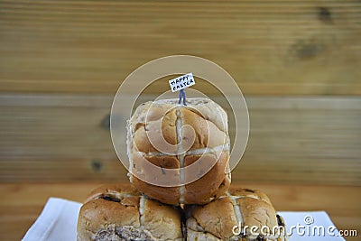 Happy Easter sign held by a miniature person figurine standing on some fresh hot cross buns Stock Photo