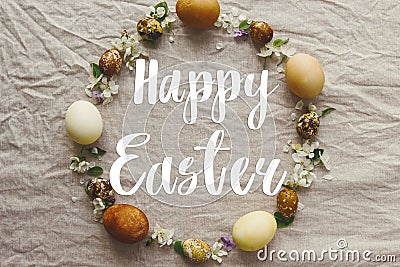 Happy Easter text on Easter eggs and spring flowers wreath on rustic linen, flat lay, handwritten sign. Beautiful stylish greeting Stock Photo