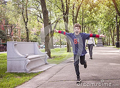 Happy eight year old boy running in a city park with arms stretched out Stock Photo
