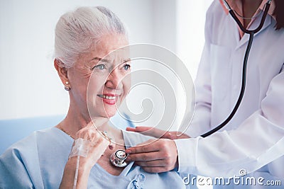 Happy Elderly patient talk with woman doctor at room in hospital. Doctor use stethoscope listening lung of elderly patient. Stock Photo