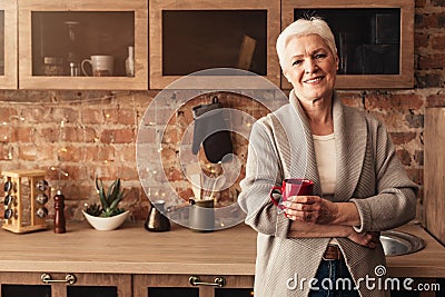 Happy elderly woman standing in kitchen with cup of coffee Stock Photo