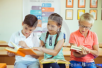 Happy elementary students sitting on desk with book and discussing in classroom Stock Photo