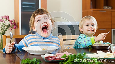 Happy emotional baby girls eating food at table Stock Photo