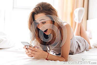 Happy emotional pretty lady lies on bed chatting by phone. Stock Photo