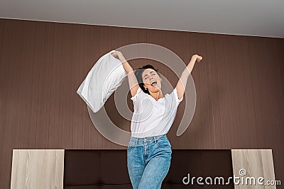 Happy emotions. A young woman sings and cheers with a pillow in her hands. Indoor. Bottom view Stock Photo