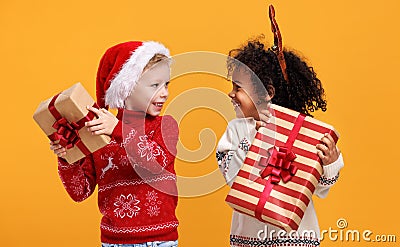 Happy excited multiracial children in Christmas outfit holding Xmas gifts against yellow background Stock Photo