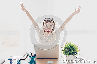 Happy excited successful businesswoman triumphing with laptop sitting at workstation workplace sitting at table in light room rais Stock Photo