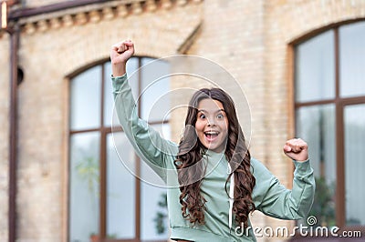 Happy excited teenage girl shouting making winner gesture in casual style blurry outdoors Stock Photo